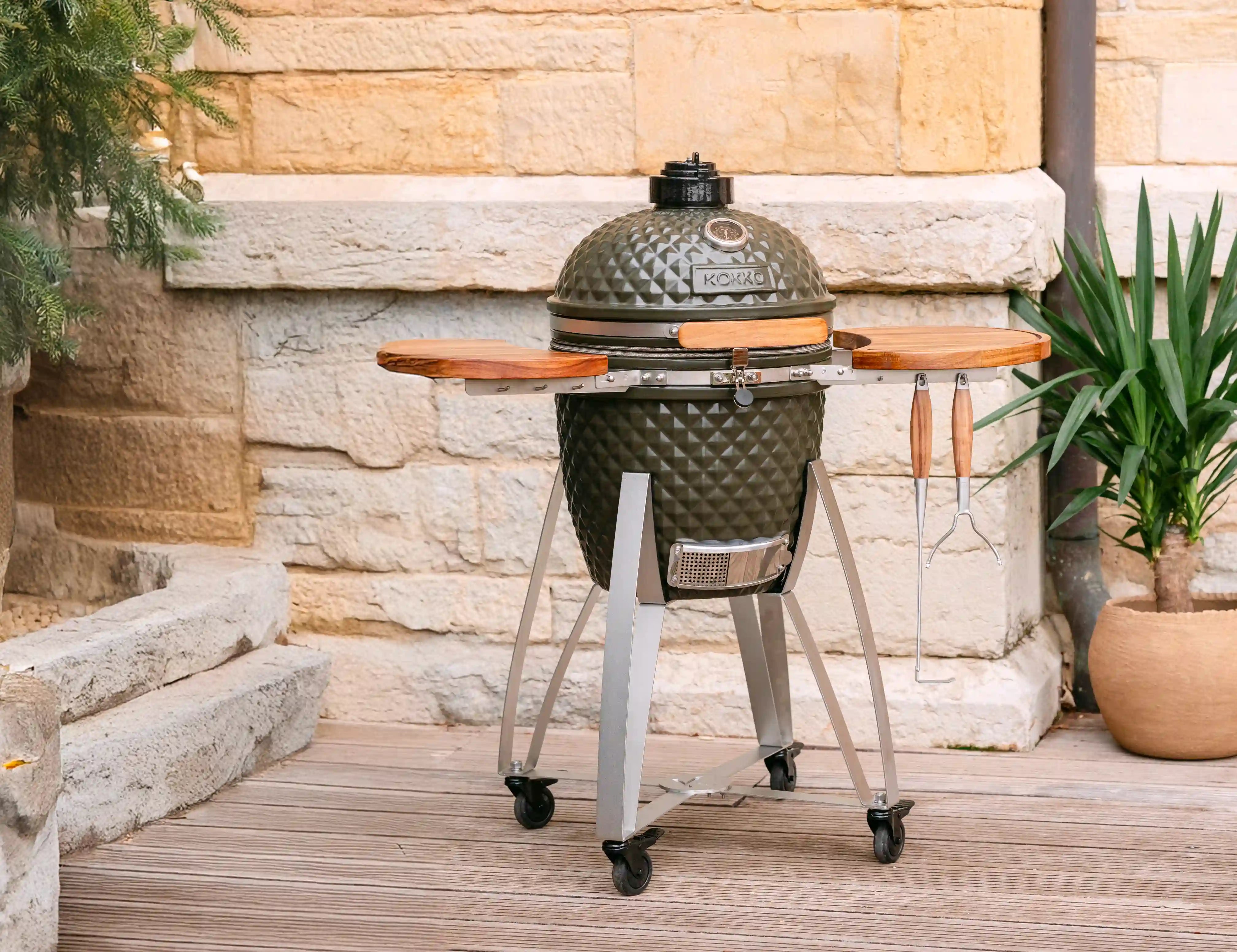 Kokko Kamado vert olive équipé de tablettes en bois et accessoires pour barbecue, idéal pour fumer, griller et cuisiner en extérieur.