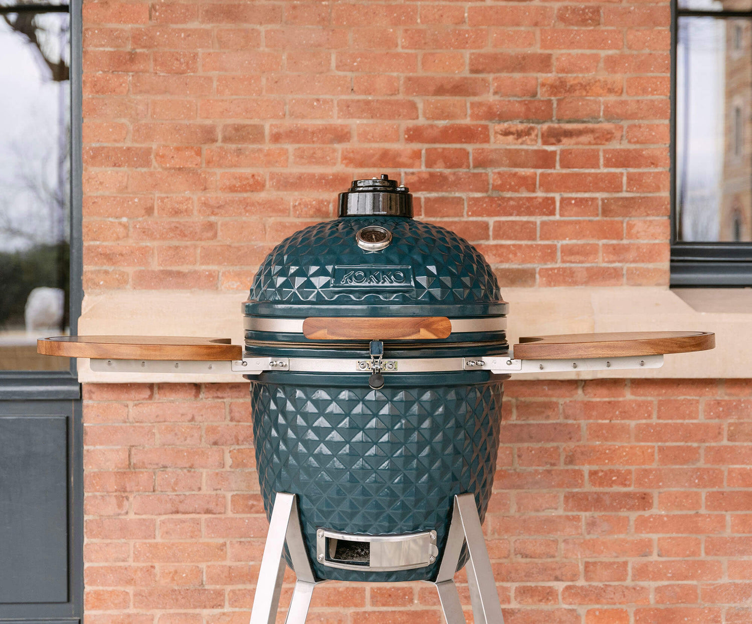 Kamado Kokko nieuwe editie op zijn trolley, met de nadruk op het design, het getextureerde keramiek en de integratie in een buitenruimte.