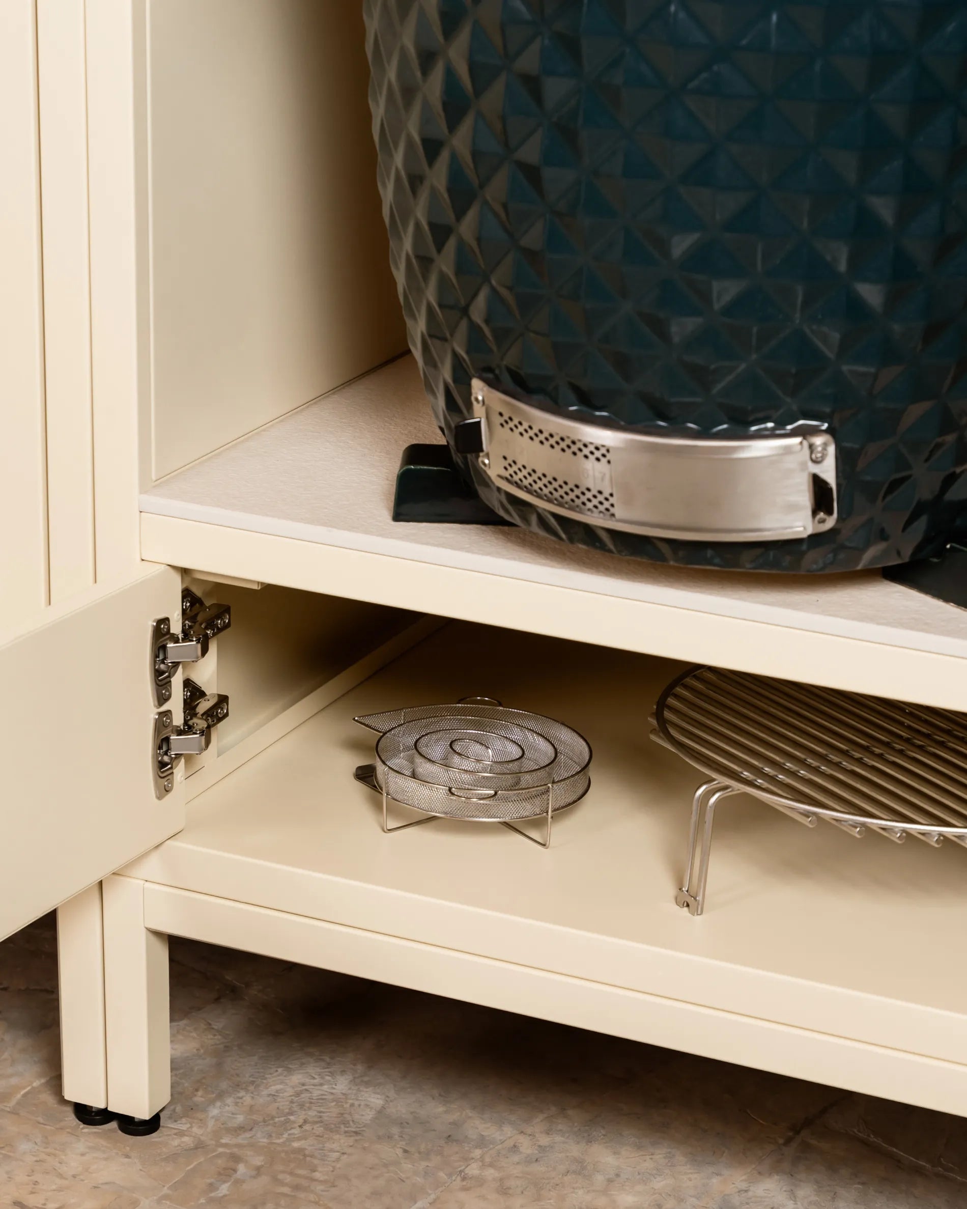 Barbecue kamado bleu marine Kokko dans niche du caisson beige crème PILOTIS, gros plan sur charnière et grilles de rangement