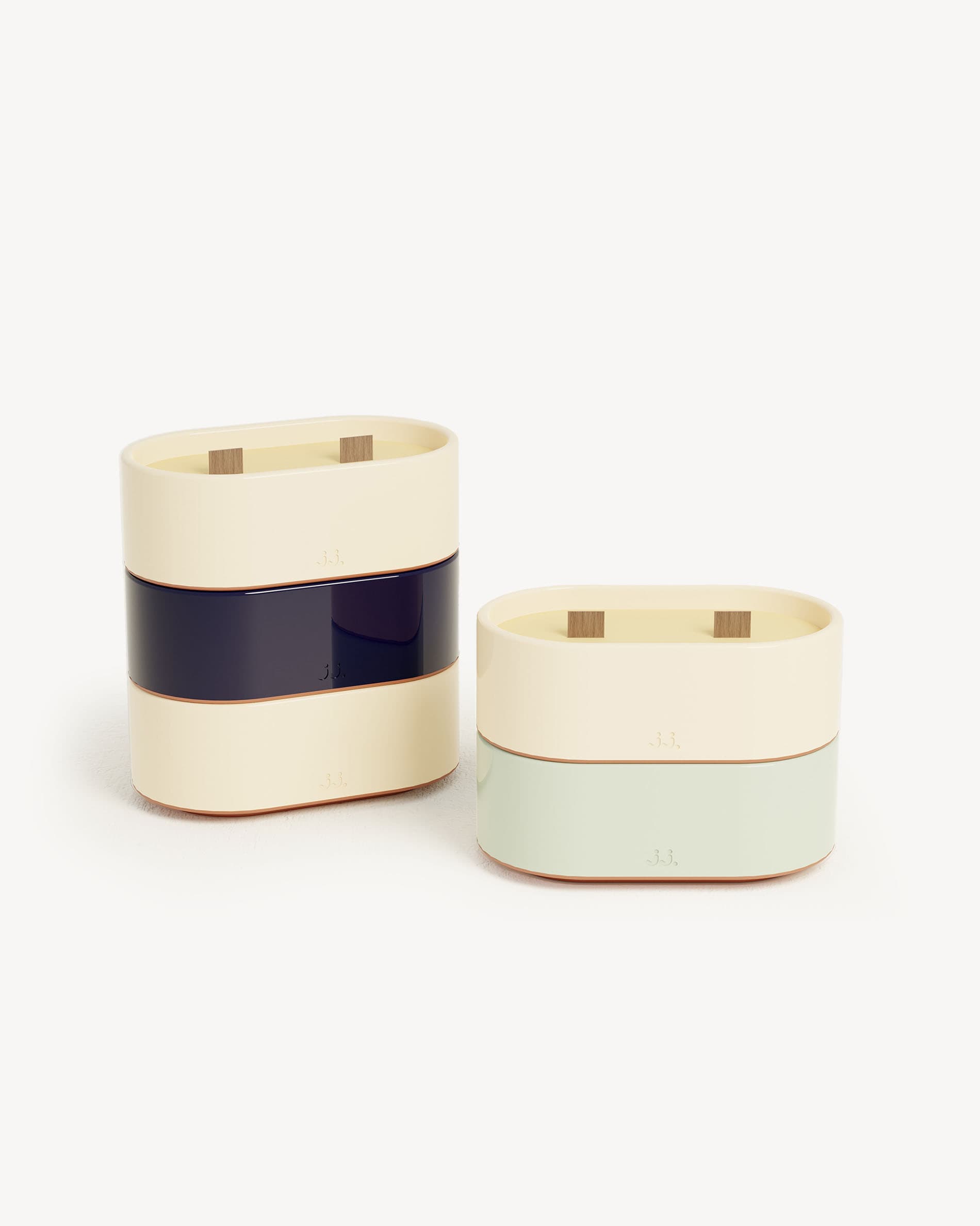 Totem S kaars van tweekleurig keramiek in ivoorbeige en marineblauw, geparfumeerd met citronella en tonen van citroen en zeezout, gepresenteerd naast een watergroene variant met eucalyptus.