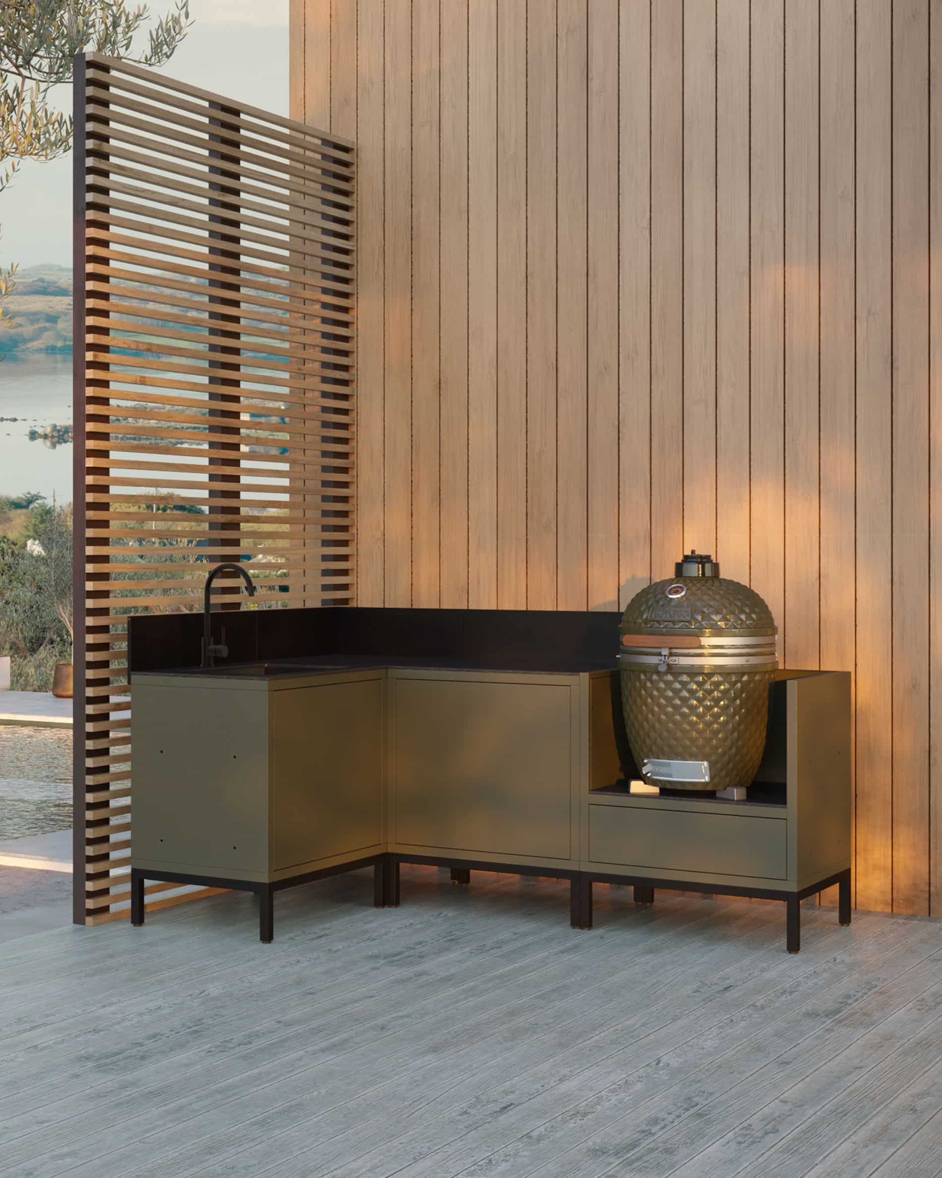 Hoekkeuken op palen in olijfgroen, bestaande uit vier modules met geïntegreerde spoelbak, zwart werkblad en een speciale plek voor de kamado, geplaatst op een houten terras tegen een verticale gevelbekleding.