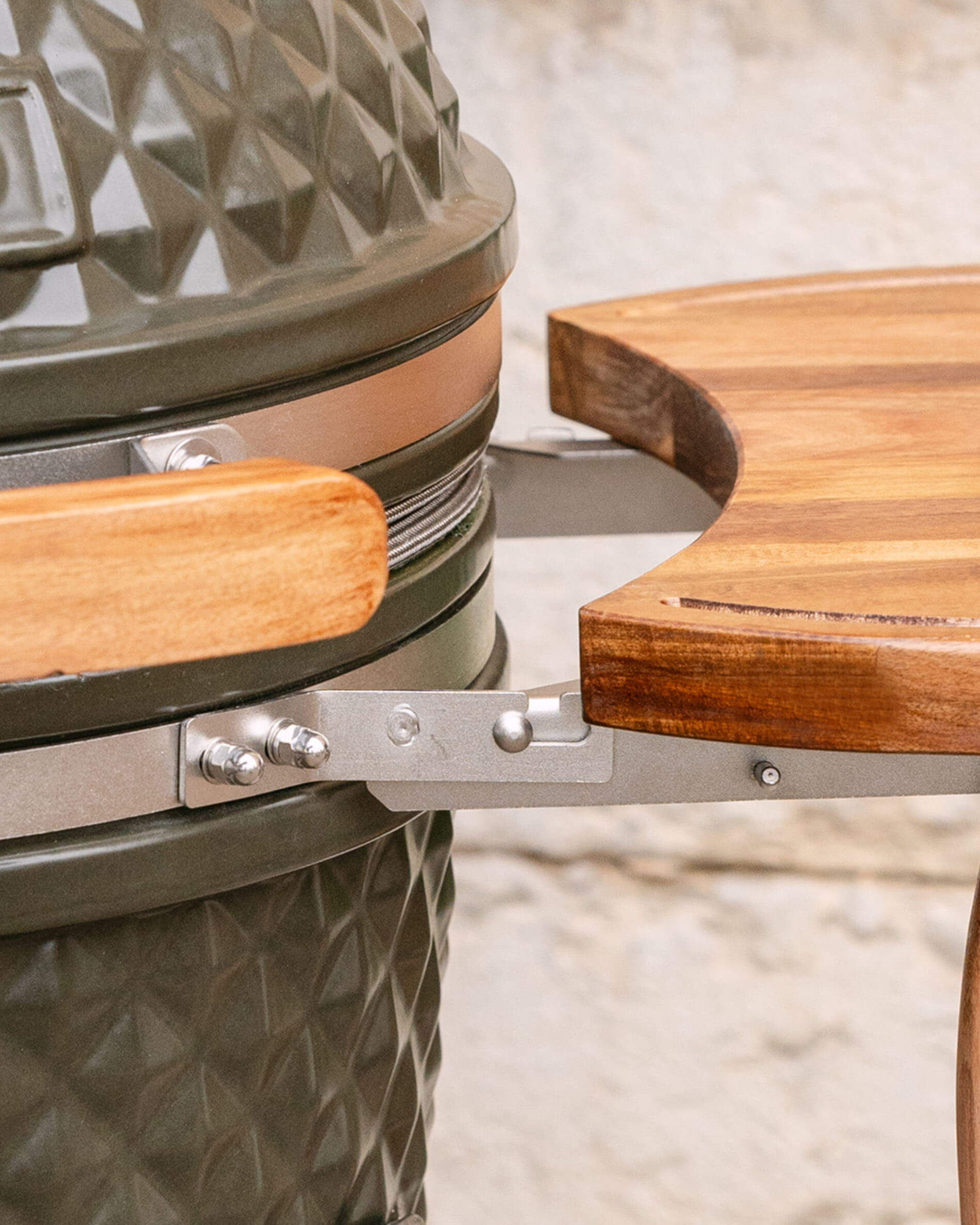 Gros plan sur la fixation métallique reliant le plateau latéral en bois au kamado, montrant le système d’accroche et la visserie.