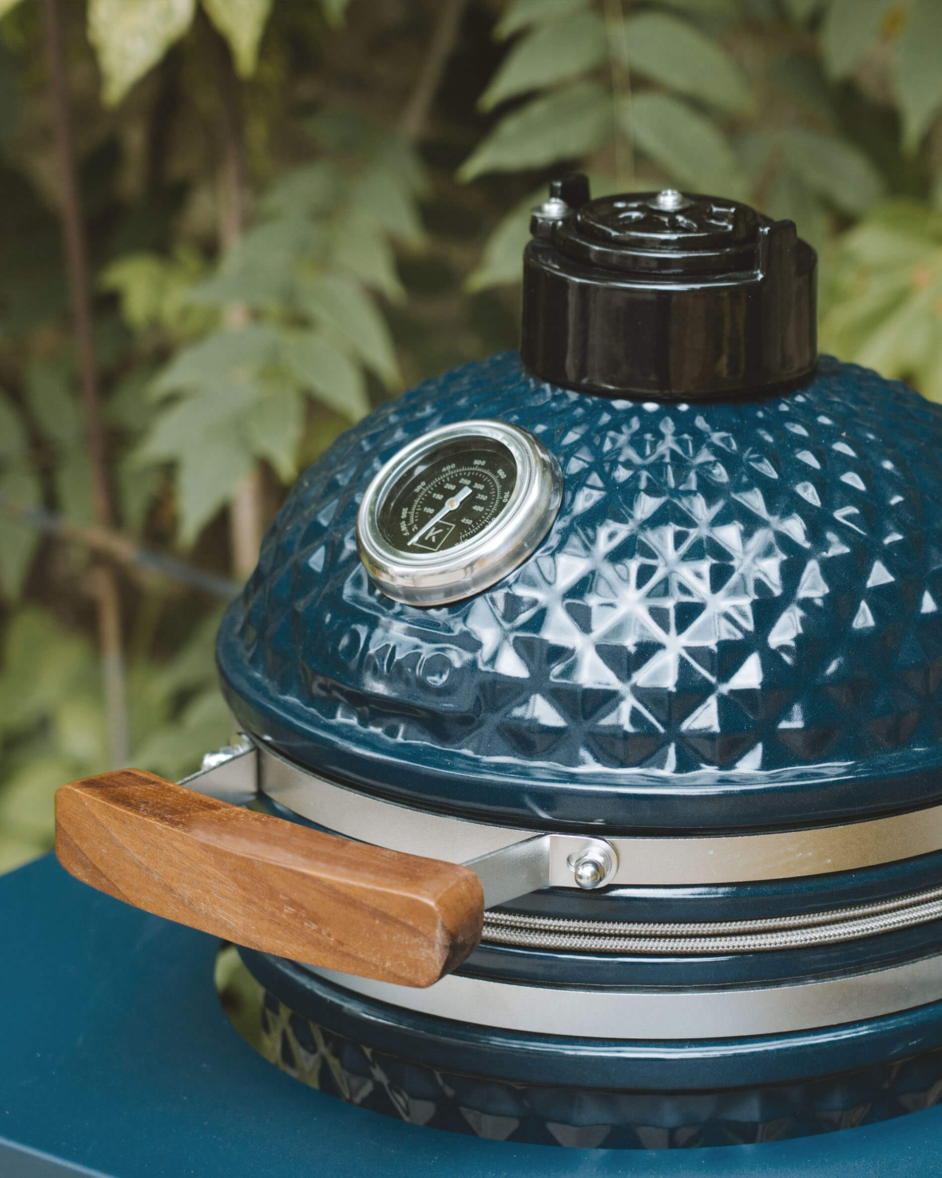 Detail van het deksel van een Kokko kamado in oceaankleur met geïntegreerde thermometer en houten handgreep.