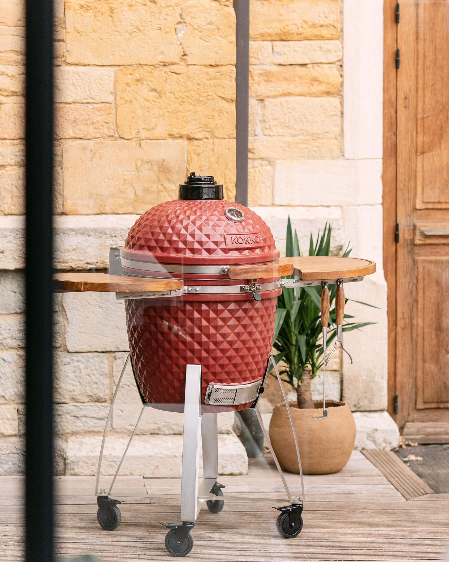 Kamado Kokko XL 22 inch in rood oxide keramiek, geplaatst op een buitenkar.