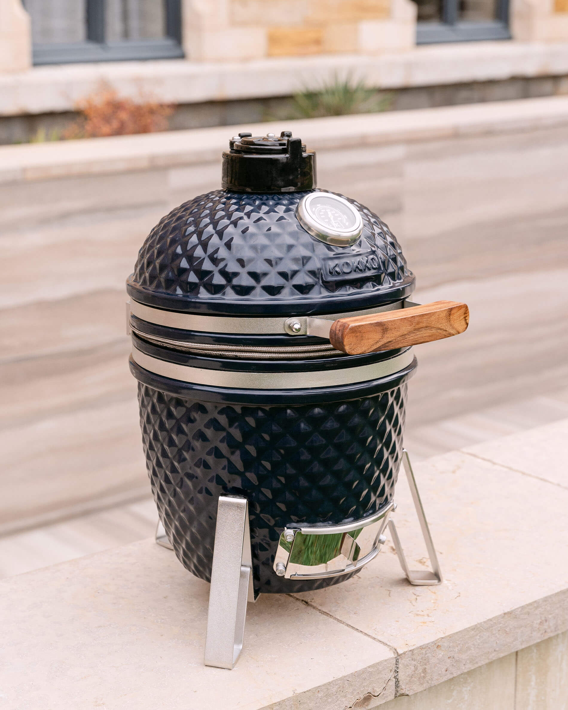 Kamado Little Kokko 13 in marineblauw, gepresenteerd op zijn onderstel in de buitenlucht.