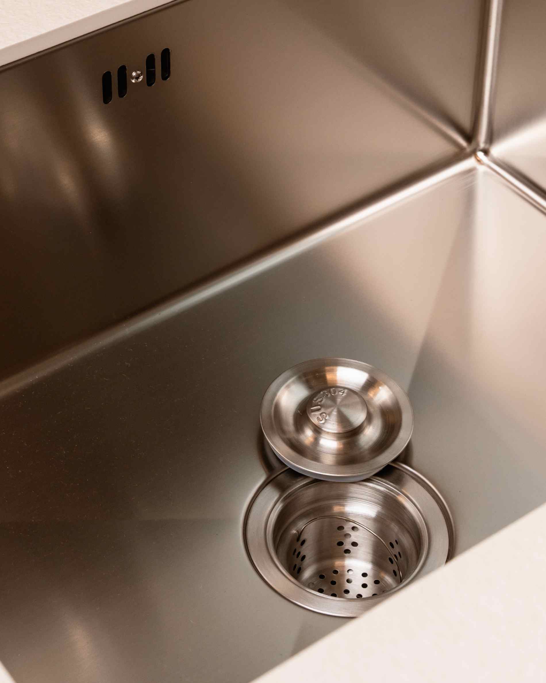 Détail de la bonde d’évier d’une cuisine pilotis, montrant le bac en inox et le système d’évacuation intégré.