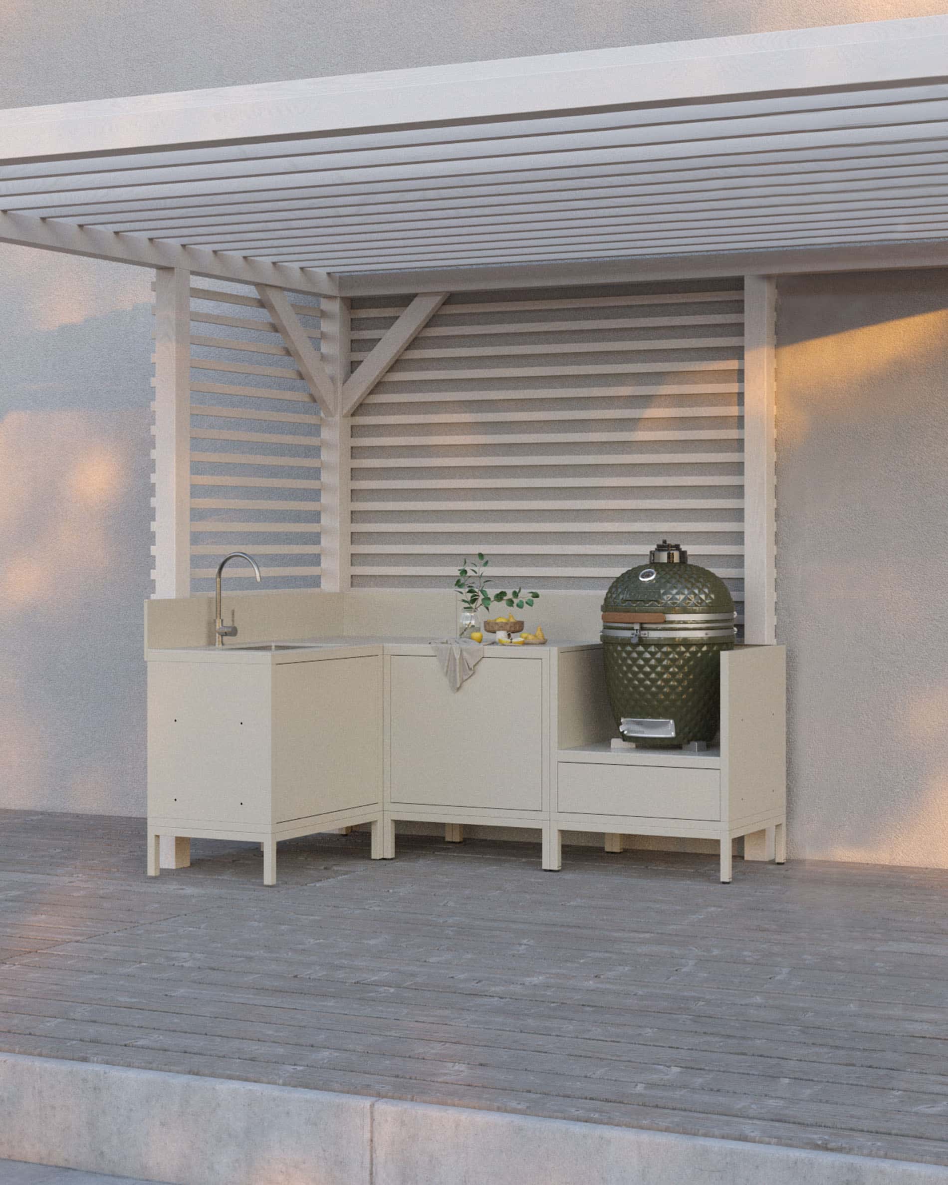 Crèmekleurige buitenkeuken op palen met vier modules, hoek en spoelbak, doorlopend werkblad en speciale plek voor de kamado, geplaatst onder een witte pergola op een houten terras.