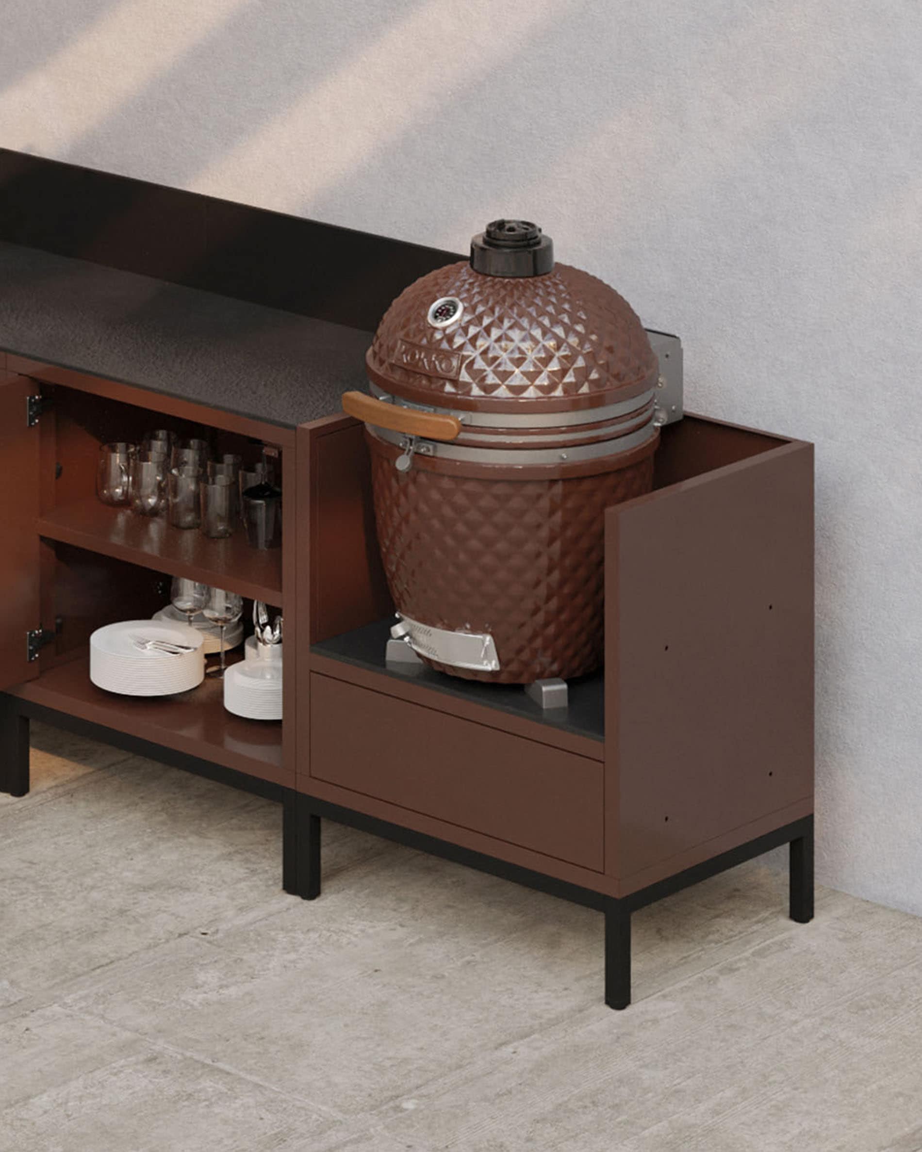 Modulaire buitenkeuken op palen in roestkleur met donker werkblad, open opbergruimte en een module ontworpen voor een kamado.