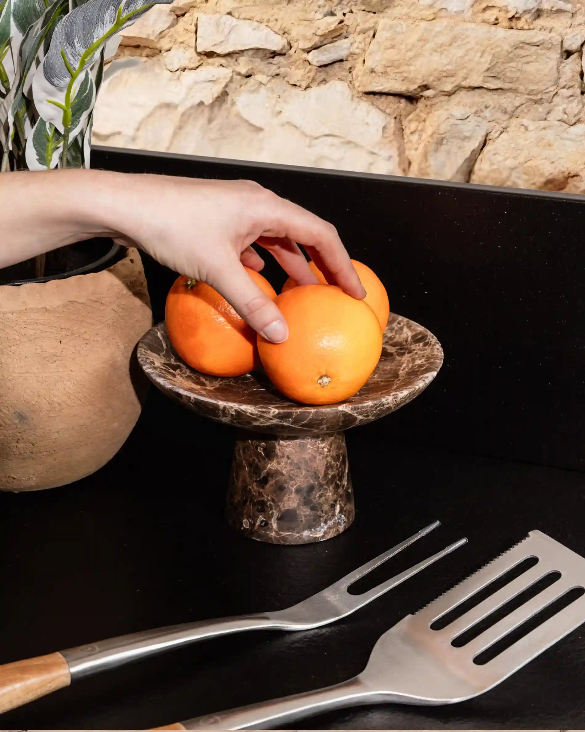 Main prenant des oranges sur un présentoir en pierre sur cuisine extérieure Kokko noire